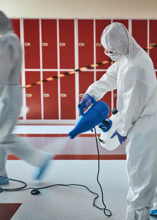 People in full body PPE spraying disinfectant in a locker room