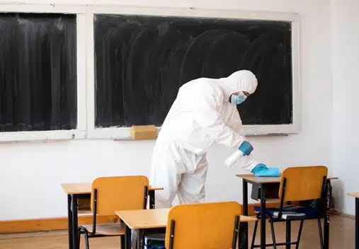 Person in full body PPE spraying disinfectant on school desks